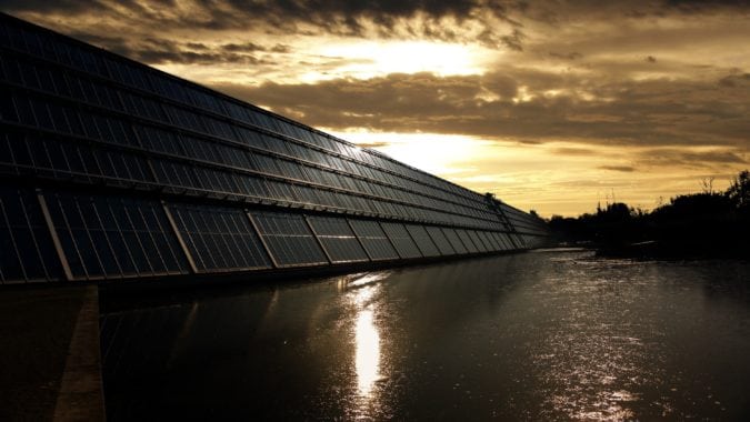 Solar panels over a body of water covered by a sunset