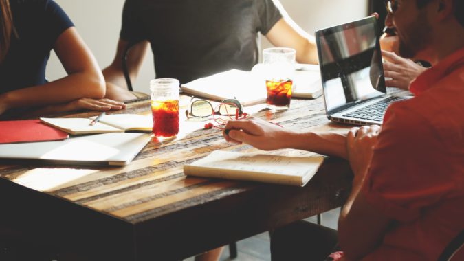 A group of co-workers are sitting at table with computers and drinks