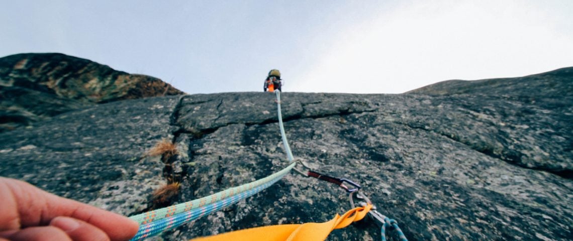 An individual is climbing a mountain while looking at their partner who just finished