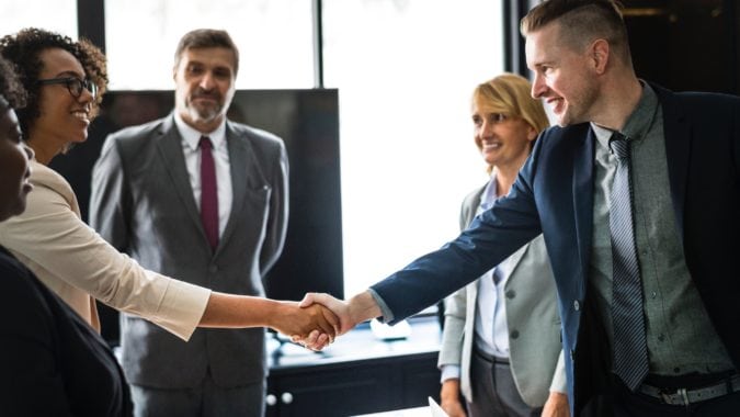 A man and woman shake hands in agreement while another man and woman watch