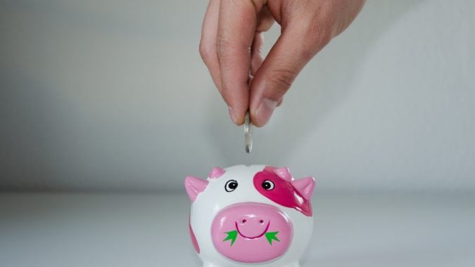 A hand is putting a coin into a piggy bank